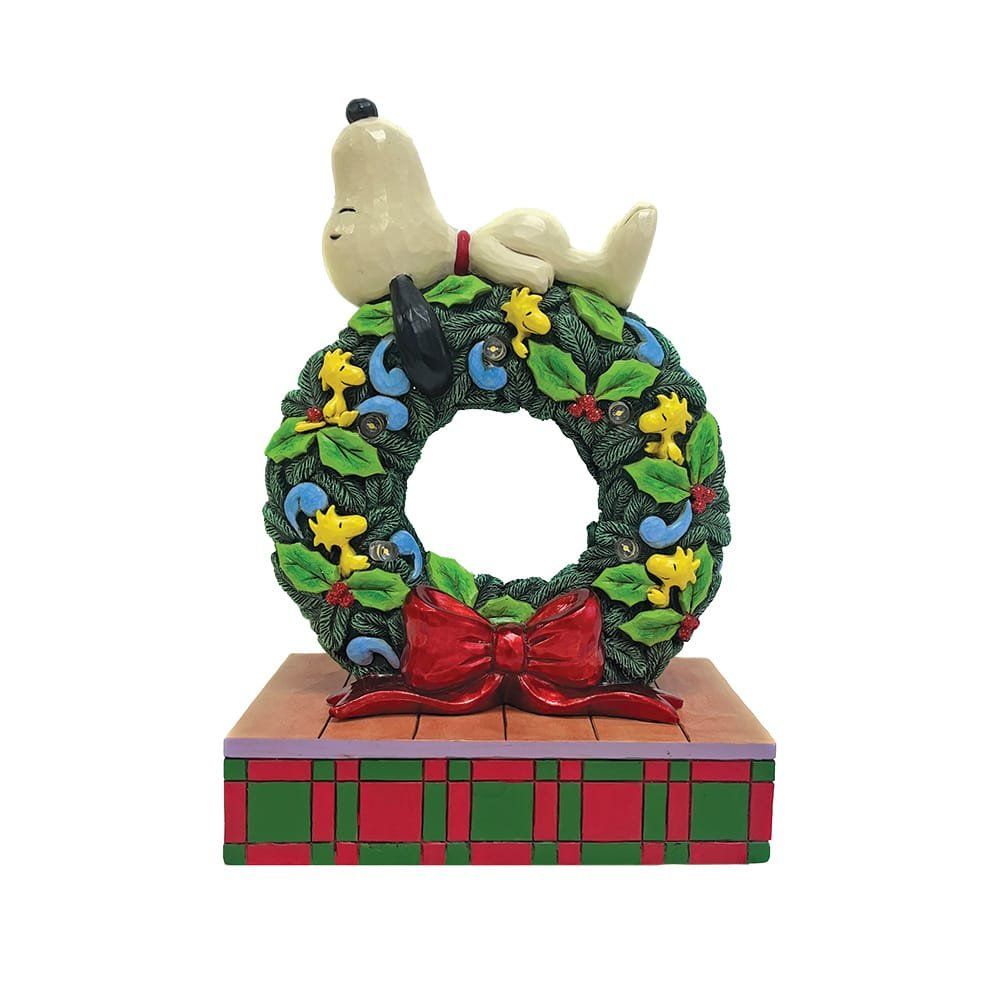 Snoopy rust op een verlichte kerstkrans met een rode strik, op een geruite blokvormige ondergrond.