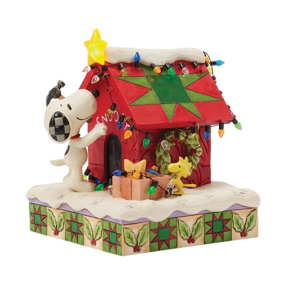 Snoopy versiert zijn rode hondenhok met kerstverlichting. Twee kleinere vogels kijken toe vanuit een geschenkdoos.
