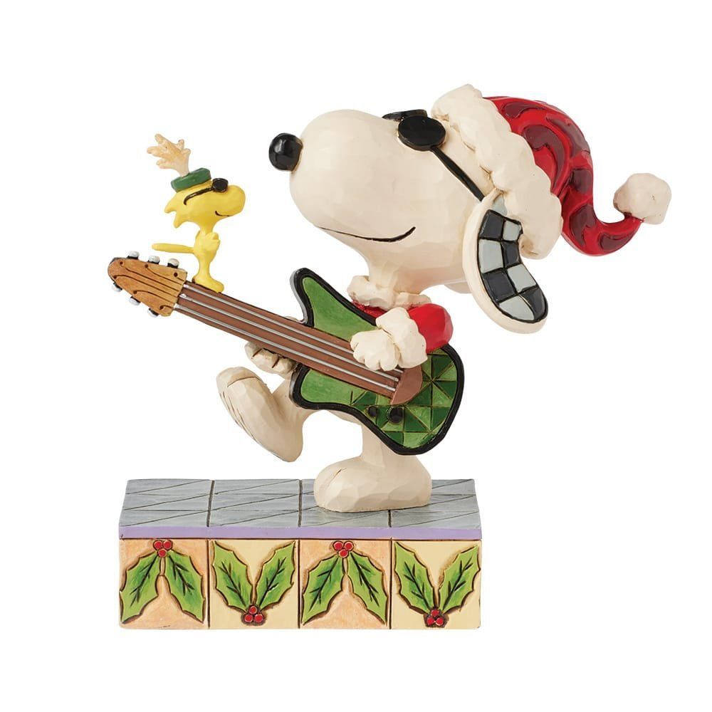 Snoopy met een kerstmuts op speelt gitaar, Woodstock erbovenop, op een podium versierd met hulst.
