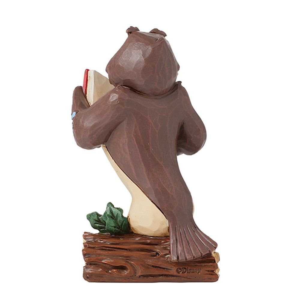 Een uilenfiguurtje dat een rood boek leest, zit op een boomstam met groene bladeren.