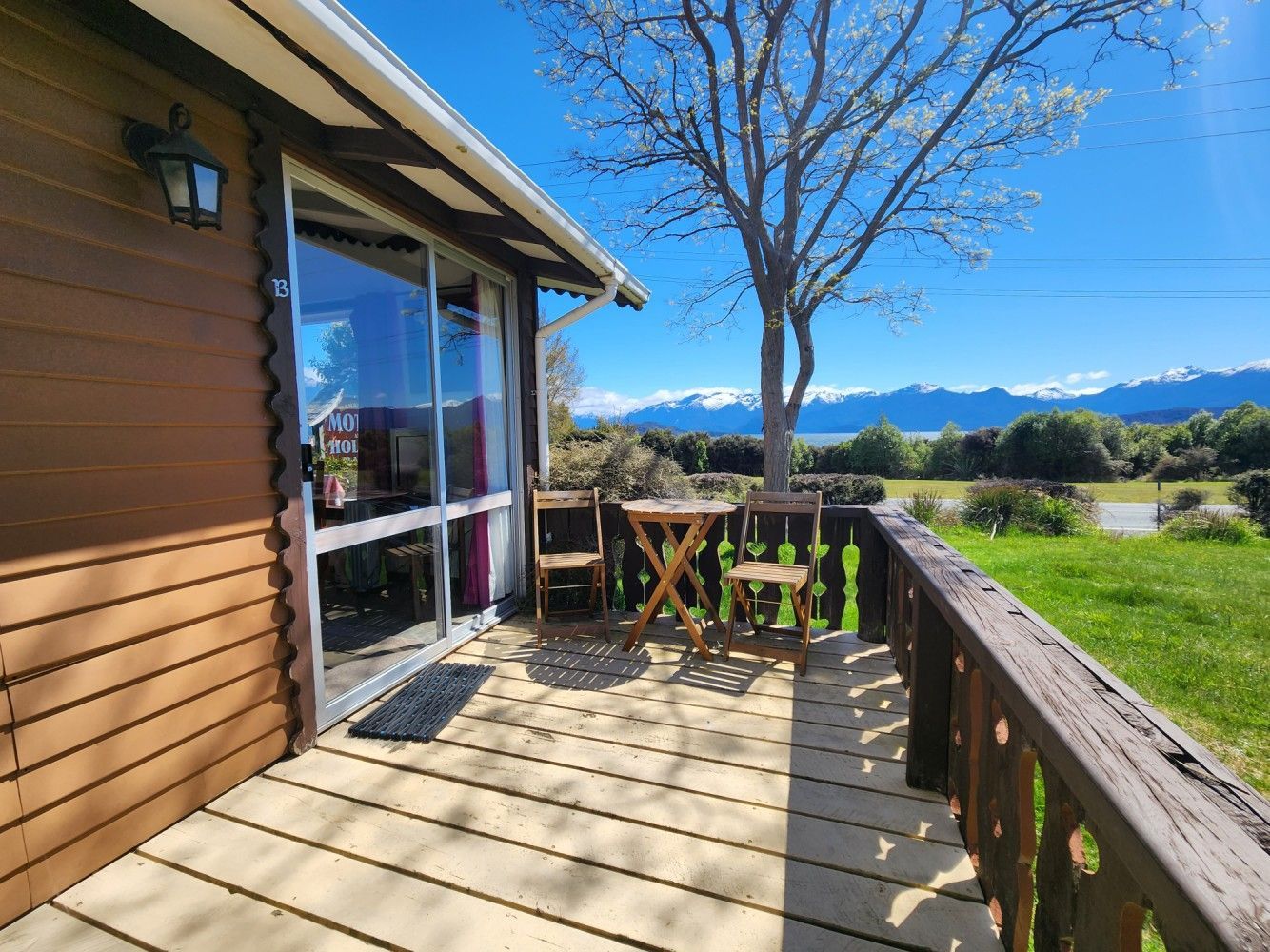 Wooden cabin with small patio, table, chairs, and scenic view of mountains and blue sky.