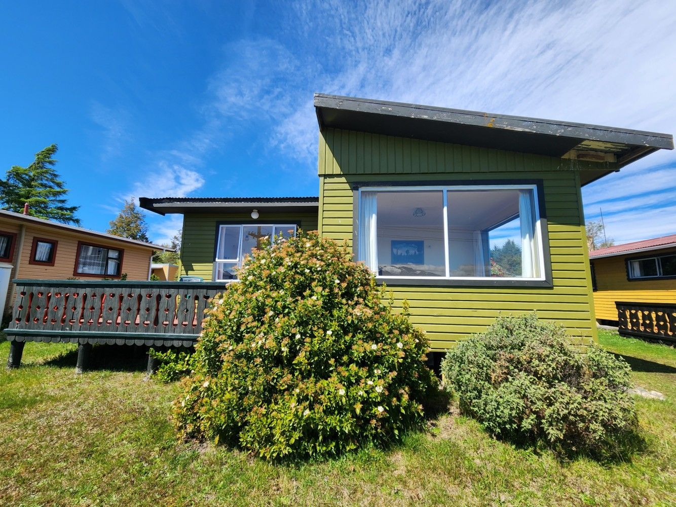 Green cabin with large windows and a small deck, set against a bright blue sky.
