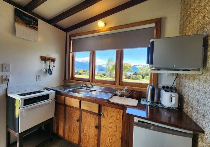 Small kitchen with a view: wooden cabinets, stainless steel sink, toaster, electric kettle, and a TV mounted on the wall.