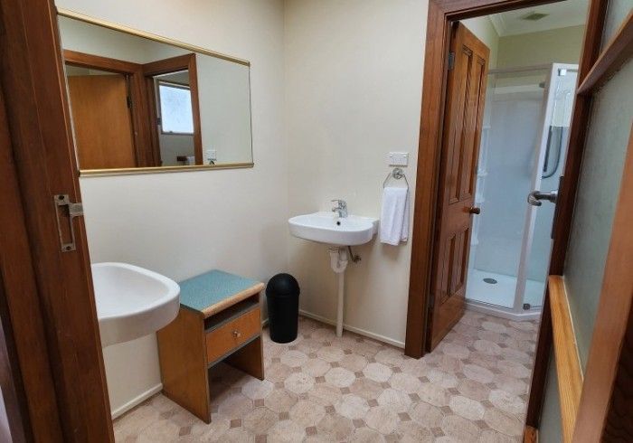 Bathroom with two sinks, a small wooden cabinet, and a shower visible through an open doorway.