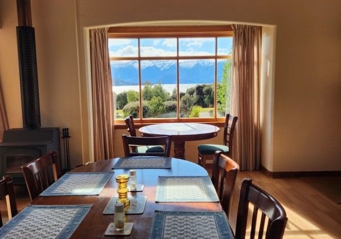 Dining room with wooden tables and chairs, large window overlooking mountains and lake.