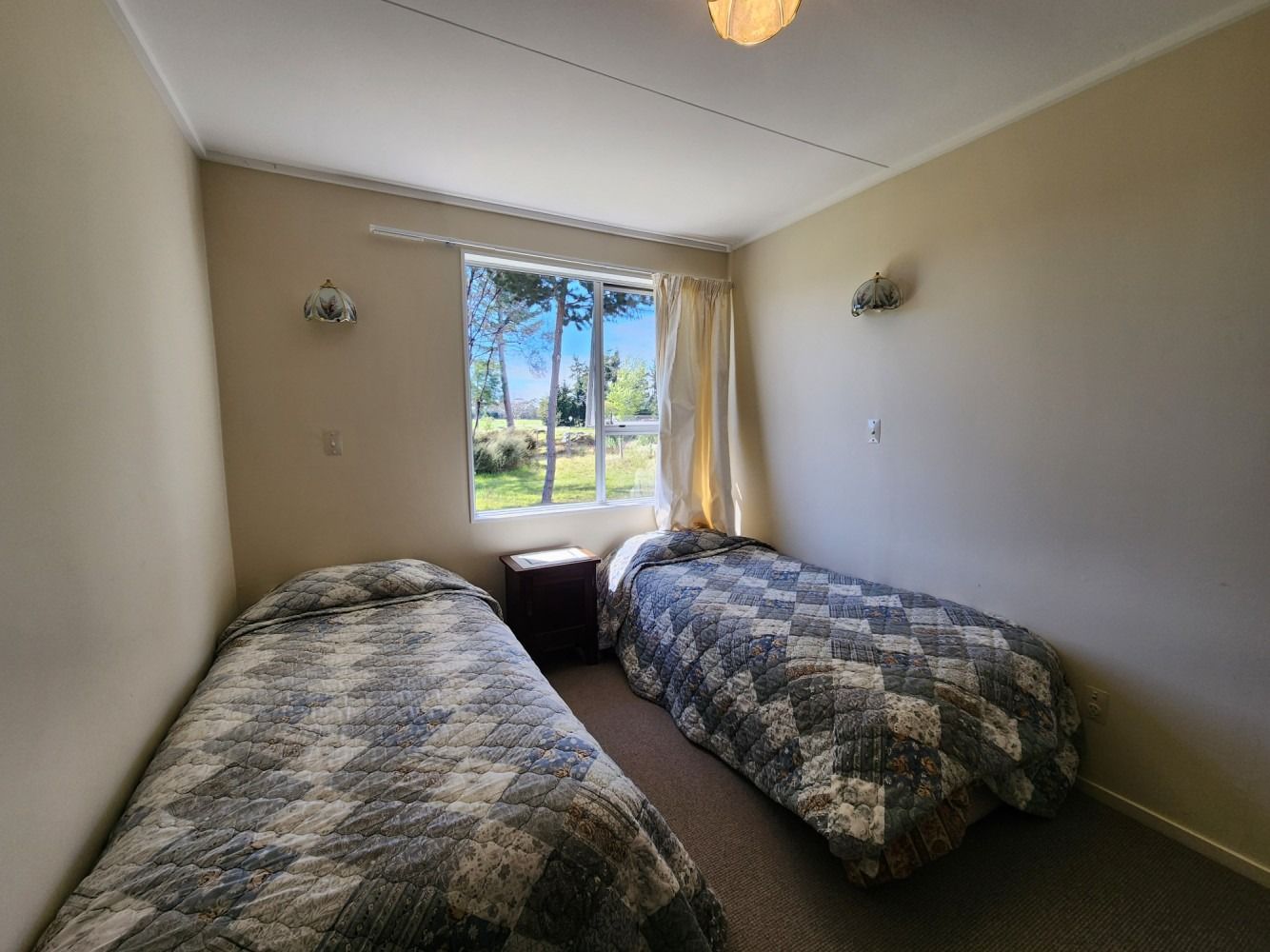 Two twin beds in a room with a window, nightstand, and beige walls.
