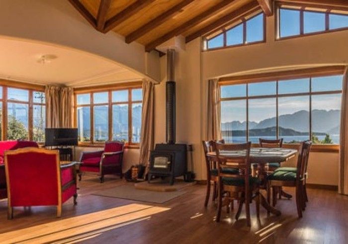 Living room with large windows, lake view, wood stove, red chairs, and dining table.