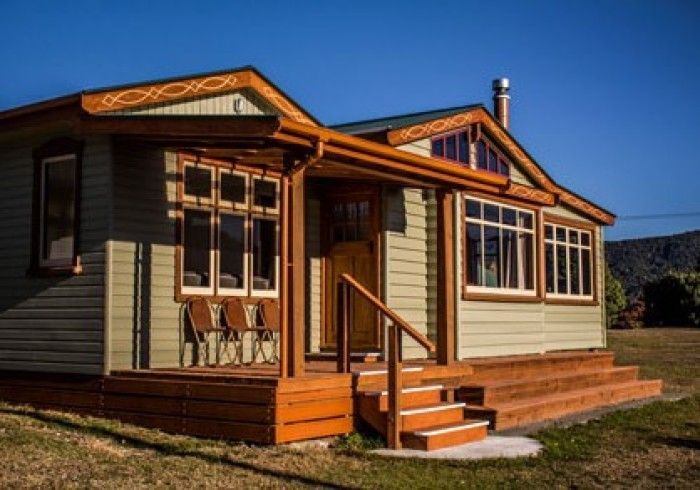 Wooden cottage with green siding, brown trim, and porch under a blue sky.