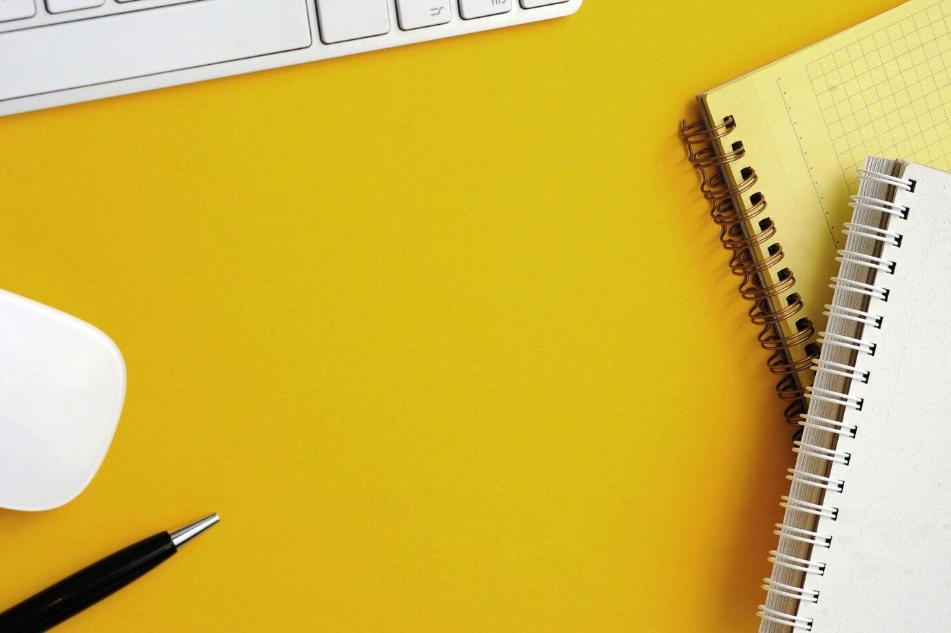 Un escritorio amarillo con un teclado, un ratón, un cuaderno y un bolígrafo.