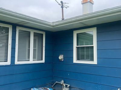 Blue house exterior corner with white-trimmed windows, a wall-mounted faucet, and a rooftop chimney.