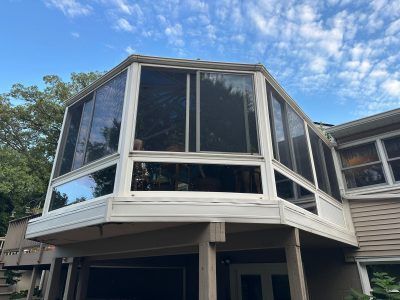 Screened porch with large windows on an elevated house exterior under a blue sky