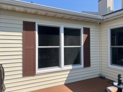 House exterior with beige siding, white-trimmed double window, and brown shutters under a blue sky