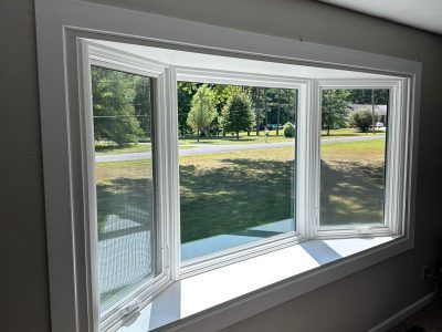 White bay window with three panes overlooking a sunny grassy yard and trees