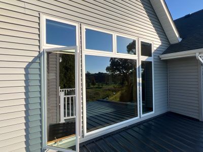 White house siding with large windows and a sliding door leading to a dark metal deck