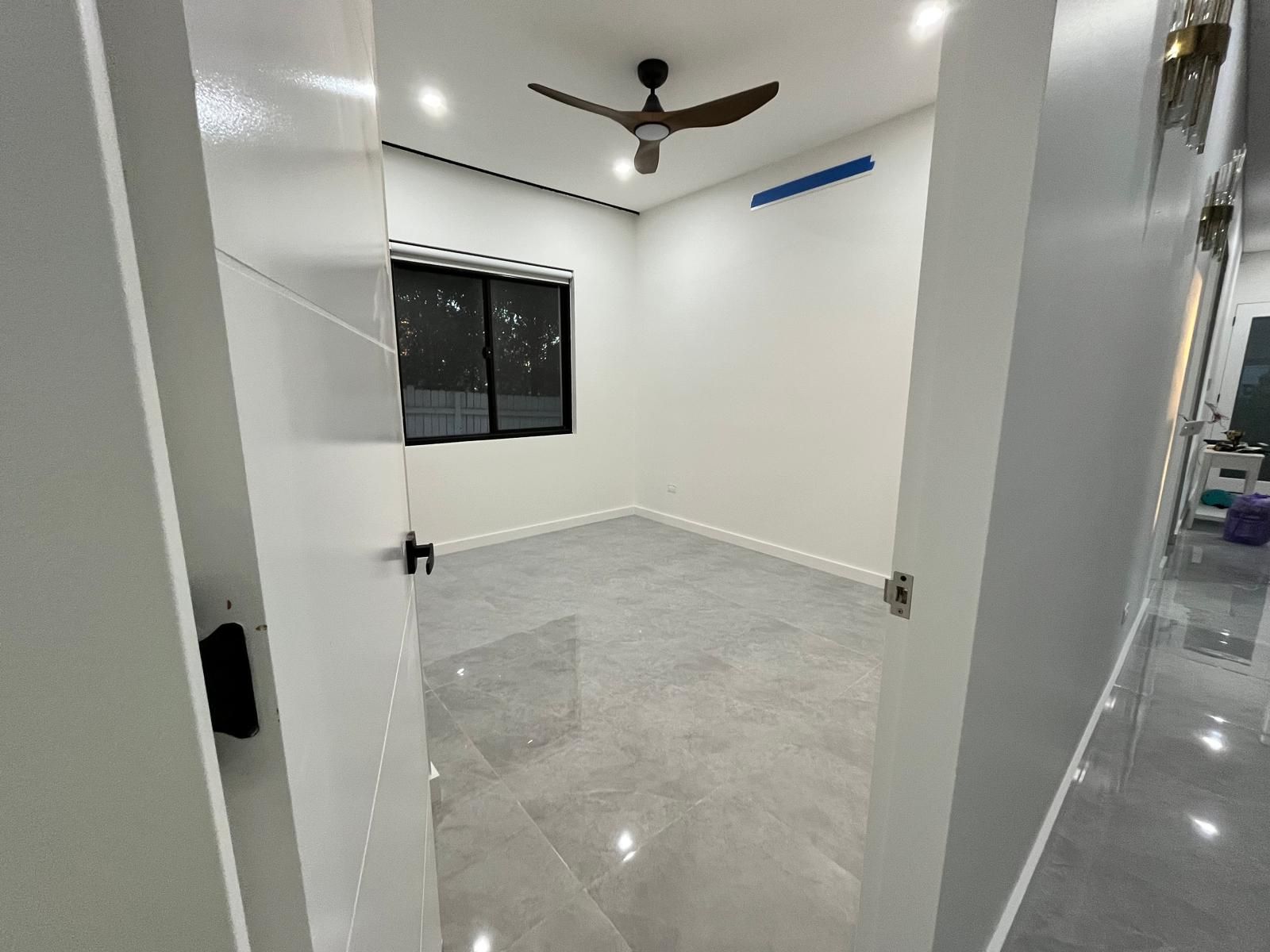Empty white room with gray tile floor, black window, ceiling fan, and open door