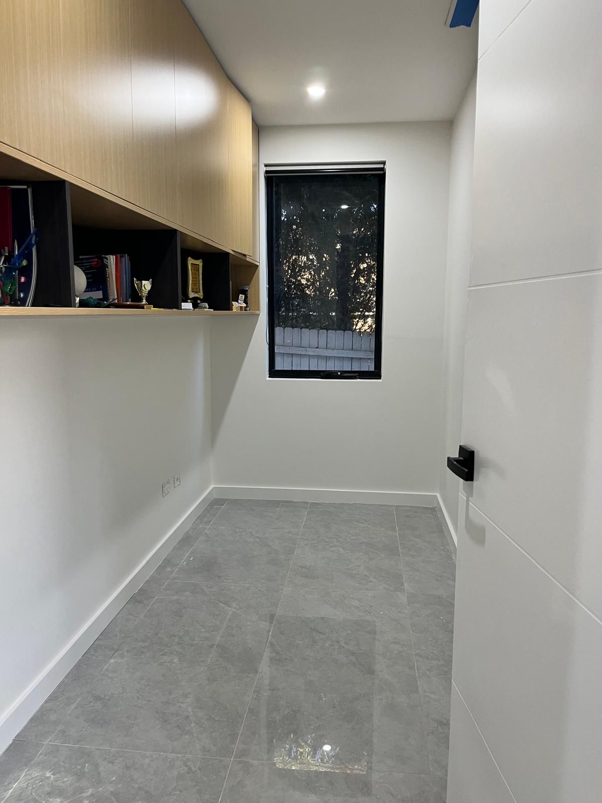 Narrow white hallway with built-in wood shelving, gray tile floor, and a window at the far end.