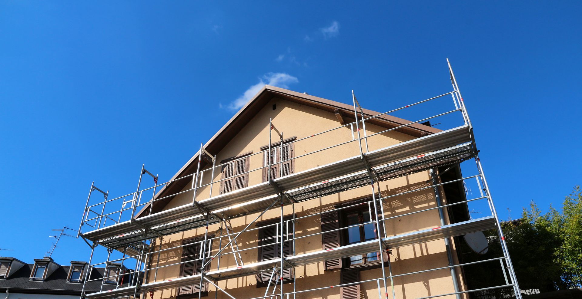 House exterior under construction with scaffolding against a bright blue sky