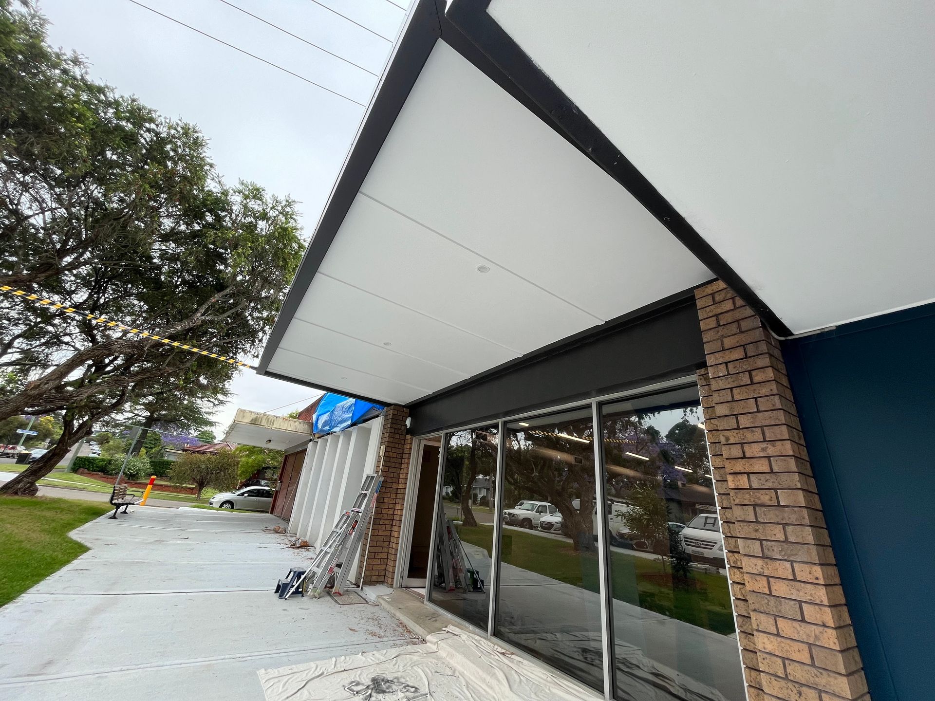 A storefront entrance featuring a large white awning, a dark brick pillar, and a blue wall under a cloudy sky. A storefront entrance featuring a large white awning, a dark brick pillar, and a blue wall under a cloudy sky.