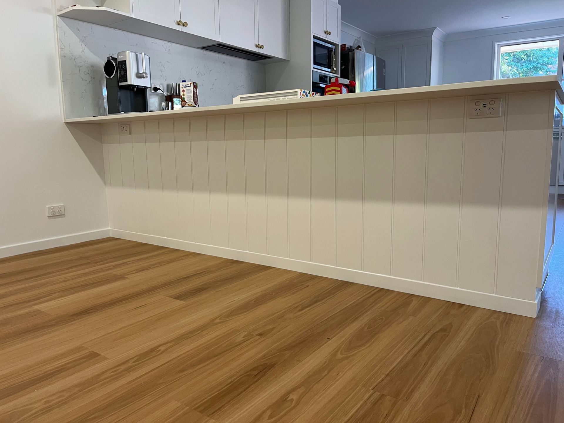 A kitchen island with white vertical paneling and a countertop, set against a wooden floor. A kitchen island with white vertical paneling and a countertop, set against a wooden floor.