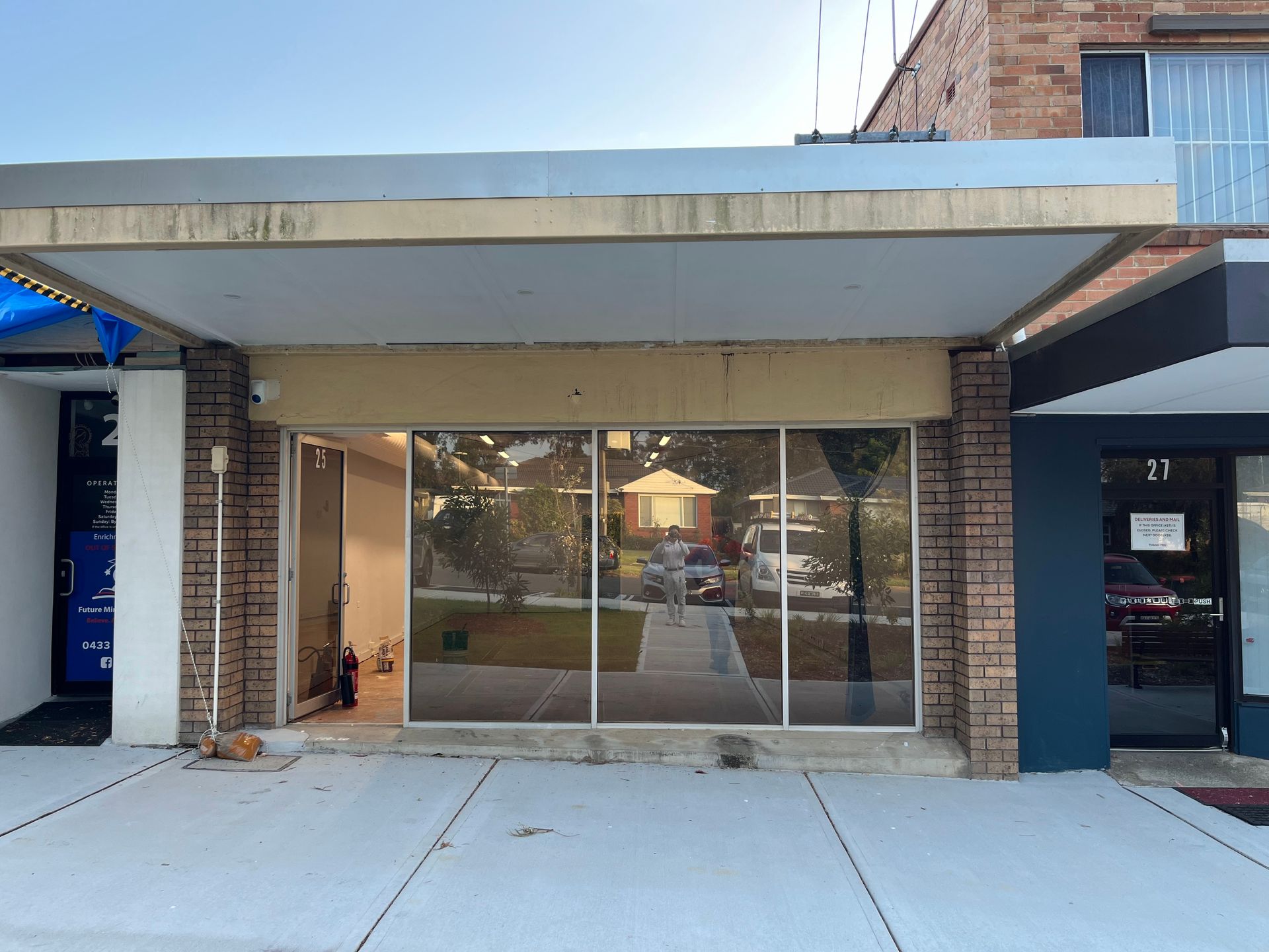 A storefront with a large glass window and metal awning, flanked by brick pillars on a sunny day.