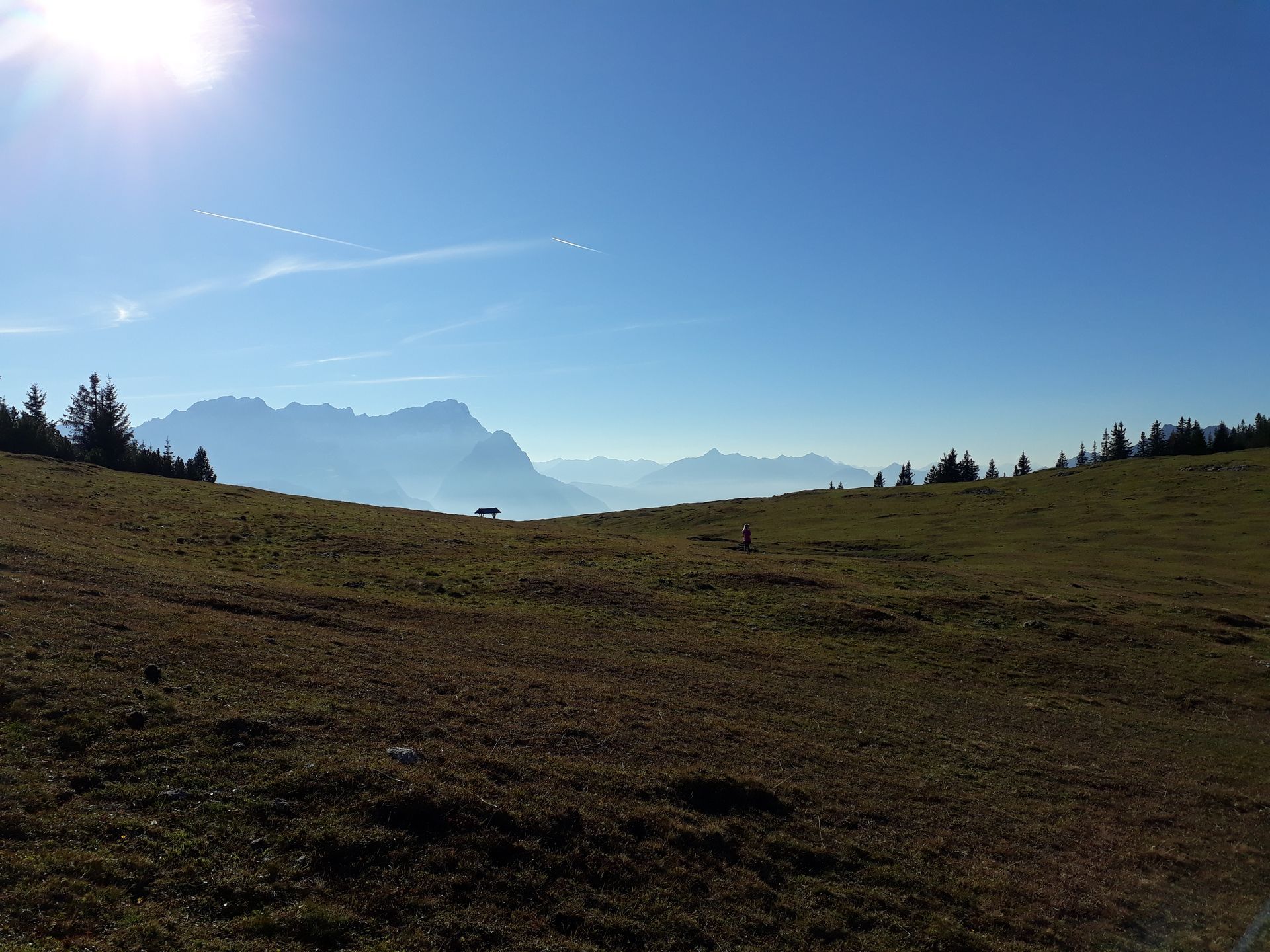 A sunny mountain landscape with a grassy field in the foreground, and hazy peaks in the distance.