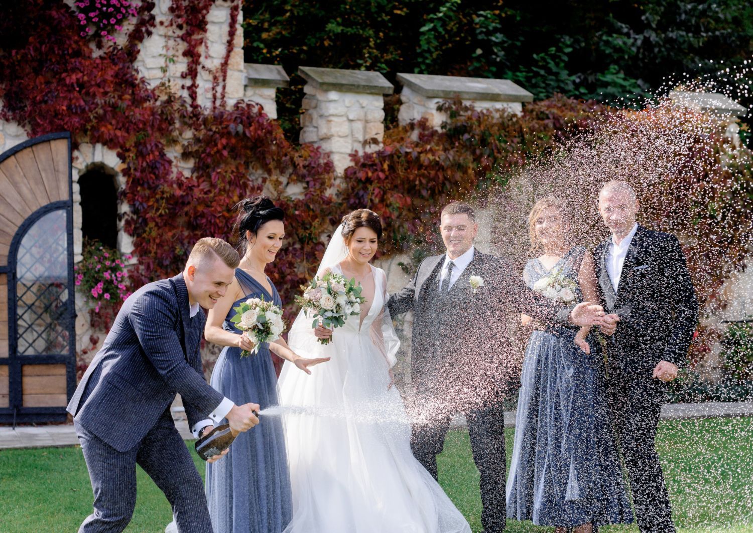 Wedding couple and guests celebrating as champagne sprays around them outdoors