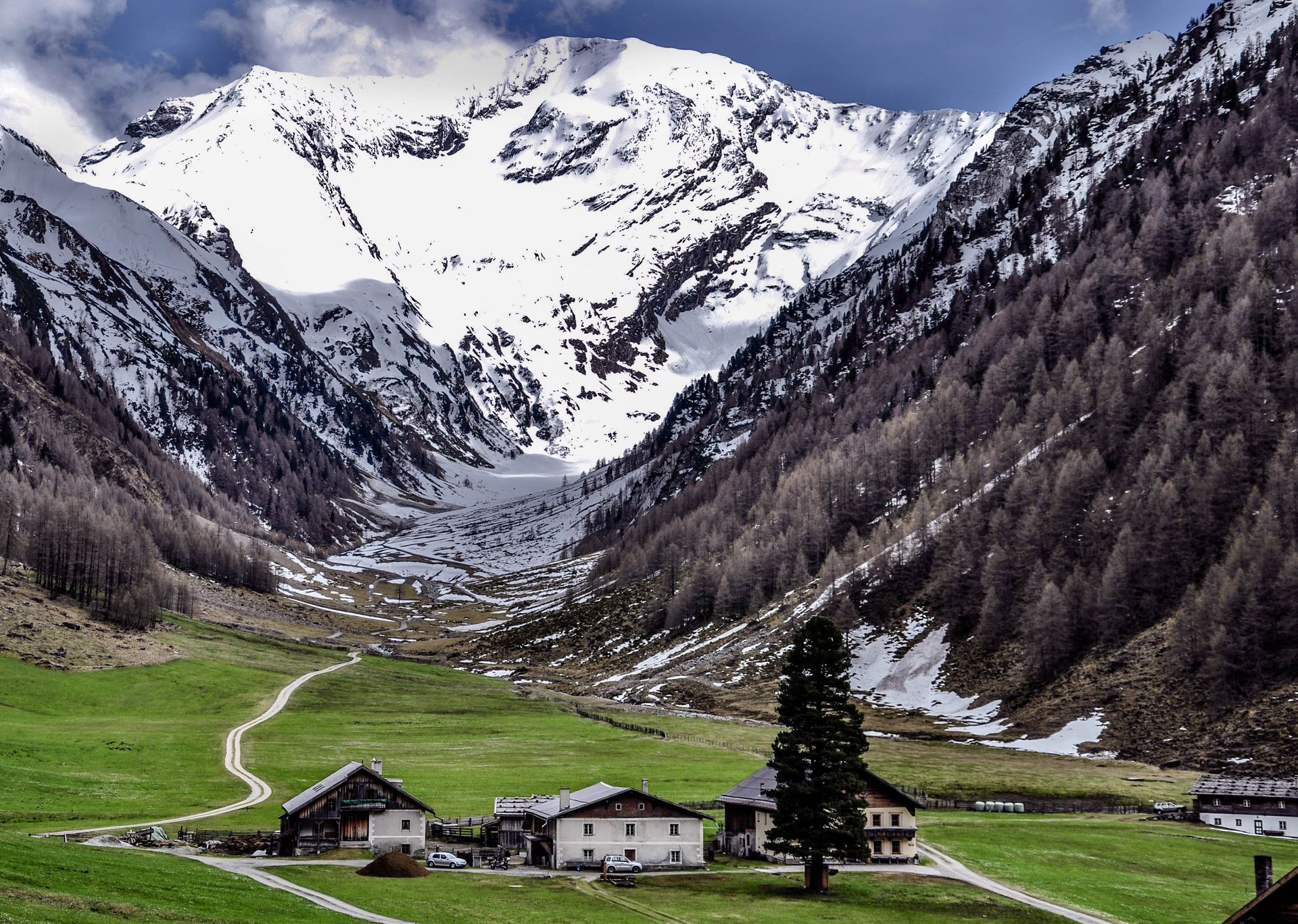 Snowy mountain valley with green meadow and small buildings.