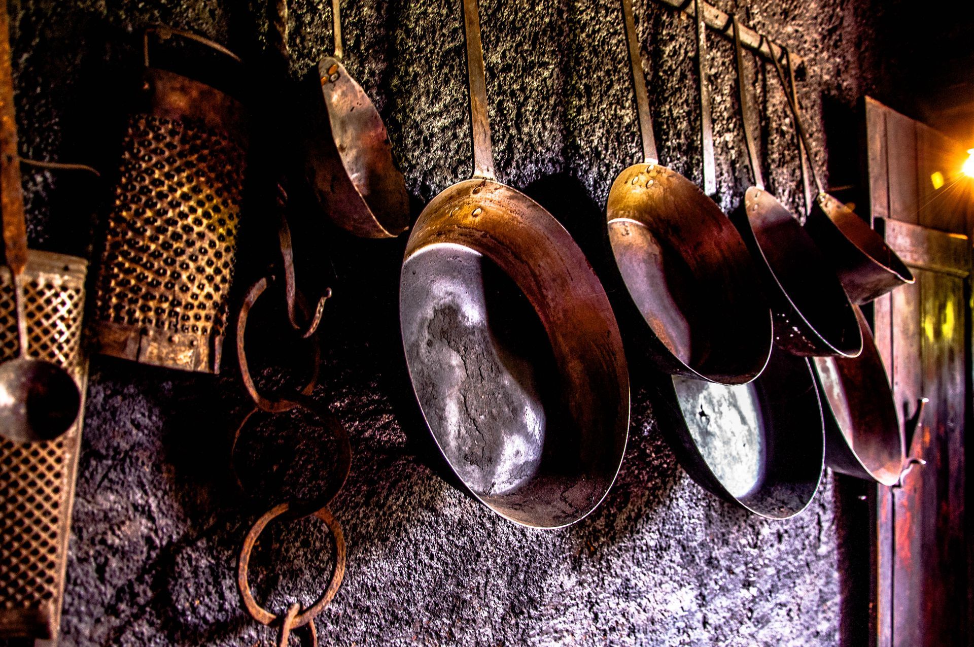 Copper pots and utensils hanging on a rough, dark stone wall.