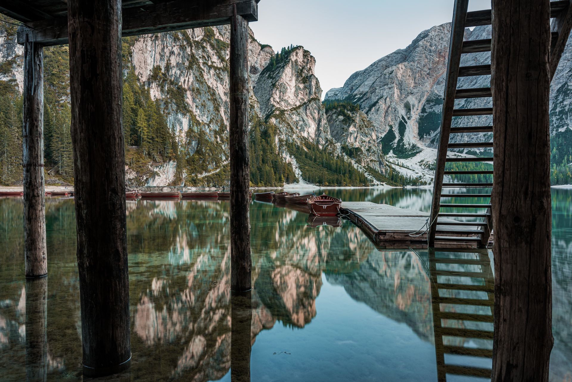 Mountain lake Lake Braies  with wooden dock and ladder, reflecting rocky cliffs and trees on calm water