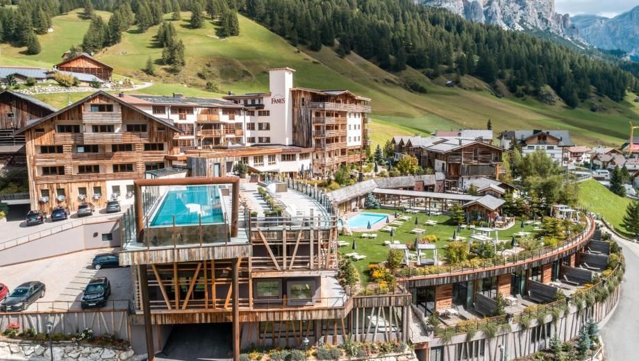 Hotel complex in mountain setting with rooftop pool, grass lawn, and parking lot.