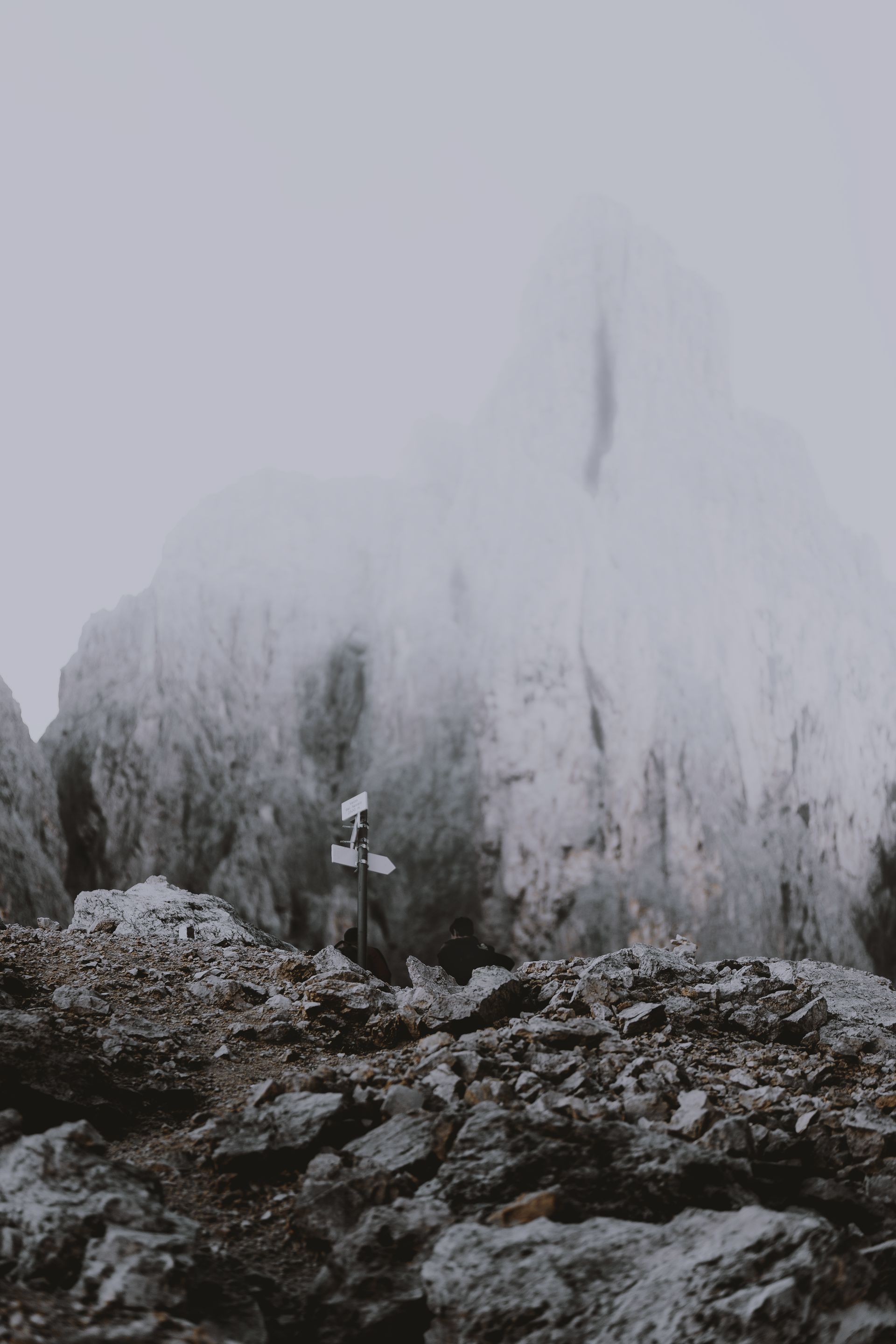 Rocky mountain peak obscured by fog; trail sign visible in foreground.