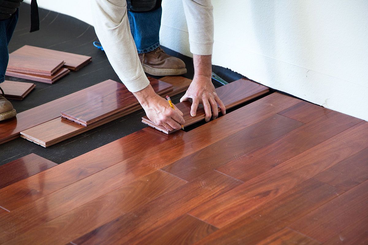 Person installing hardwood flooring; brown wood planks, pencil, measuring. Person installing hardwood flooring; brown wood planks, pencil, measuring.