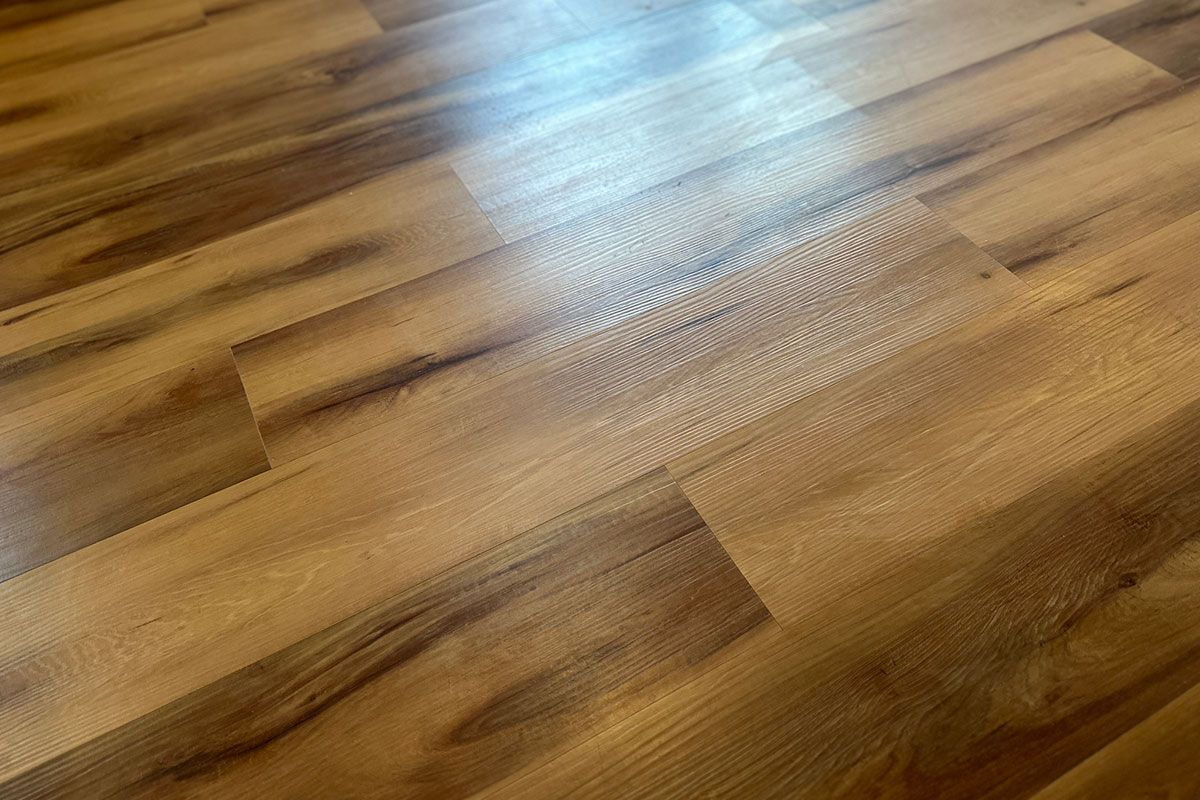 Close-up of a light-brown wood-look floor with a textured surface. Light reflects off the planks. Close-up of a light-brown wood-look floor with a textured surface. Light reflects off the planks.