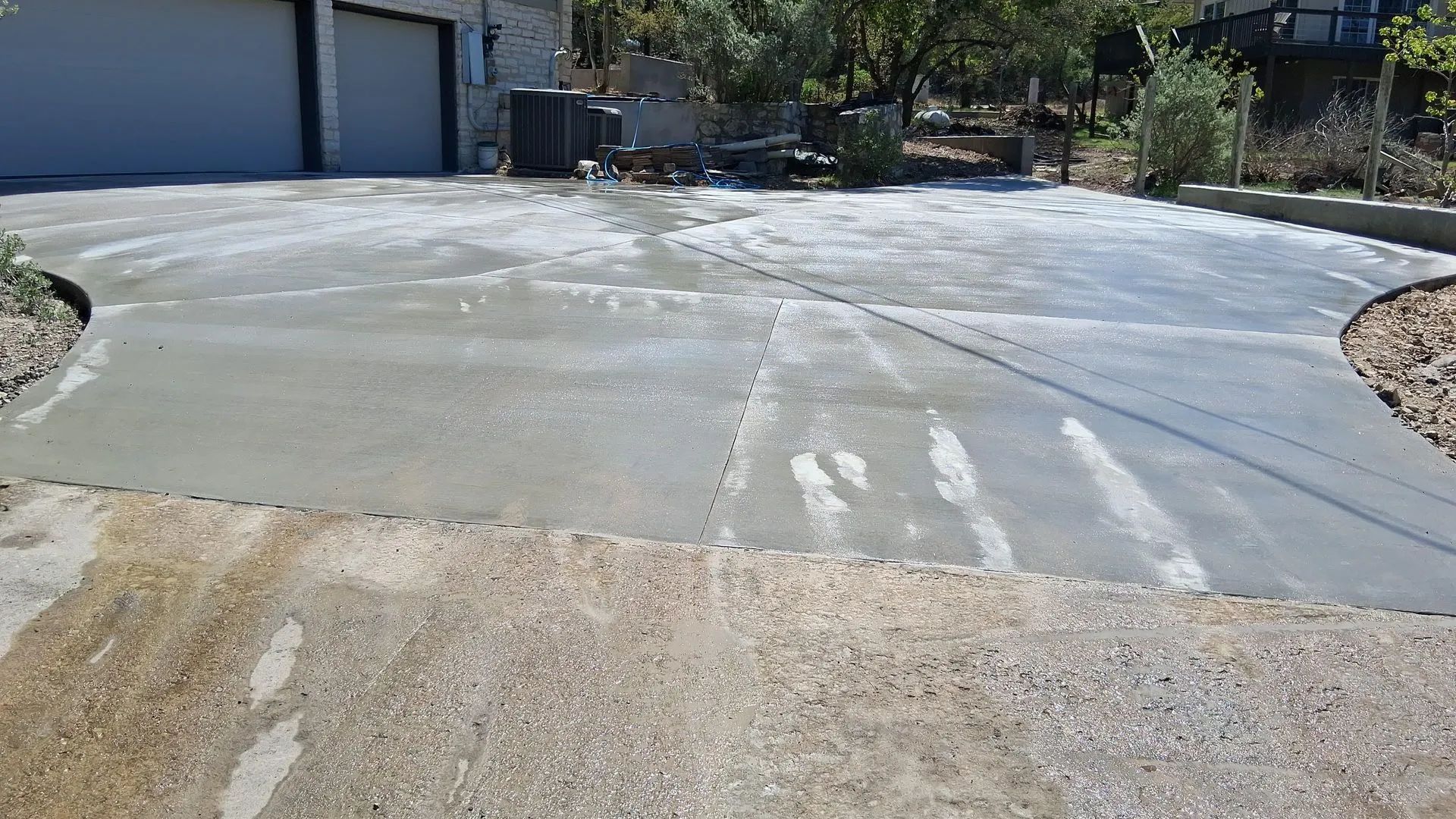 Concrete driveway being poured and smoothed near a garage on a sunny day