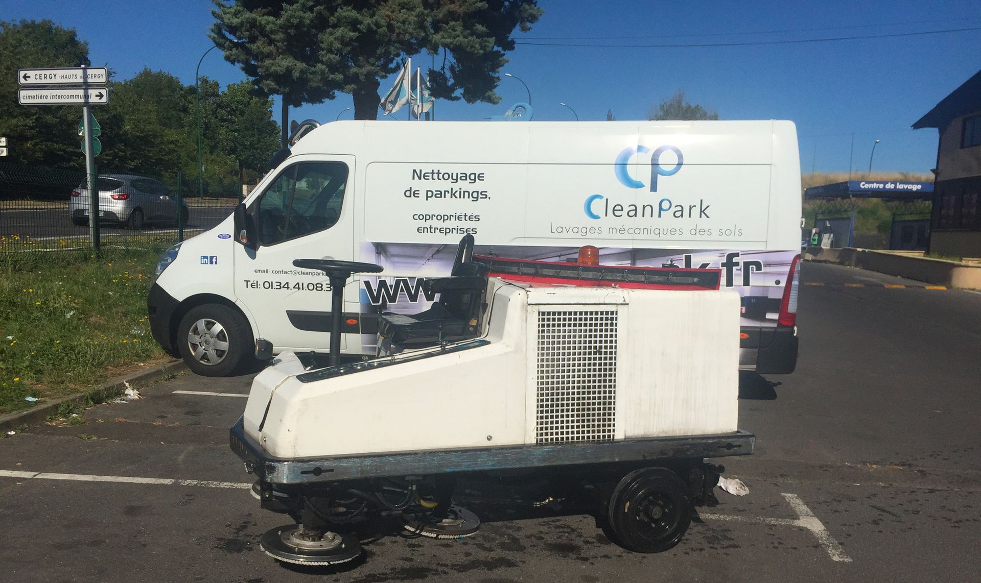 Chariot utilitaire blanc garé devant une camionnette de livraison blanche dans une rue ensoleillée, bordée d'arbres et de bâtiments.