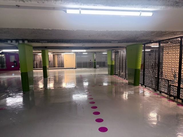 Un parking souterrain vide, avec des colonnes vertes et une rangée de points roses au sol qui s'étend au loin.