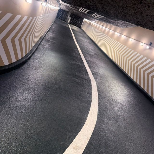 Tunnel souterrain avec une route noire sinueuse et des murs blancs à chevrons éclairés par des lumières zénithales