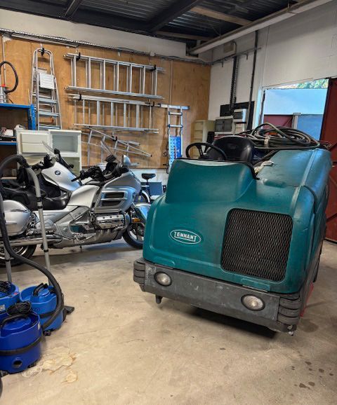 Un triporteur cargo turquoise et une moto argentée dans un atelier-garage avec des outils accrochés au mur