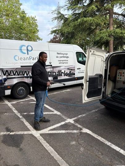 Un homme se tient debout sur un parking à côté d'une camionnette de service blanche aux portes ouvertes, portant le logo CleanPro.