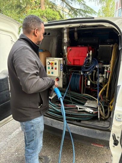 Un technicien inspecte un équipement à l'arrière d'une camionnette d'intervention, tenant un tuyau bleu et un panneau de commande.