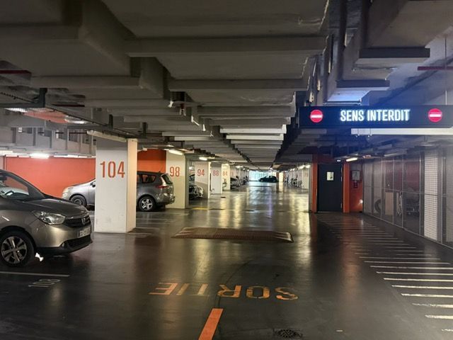 Parking intérieur avec voitures, piliers numérotés et une enseigne SENS INTERIOR.