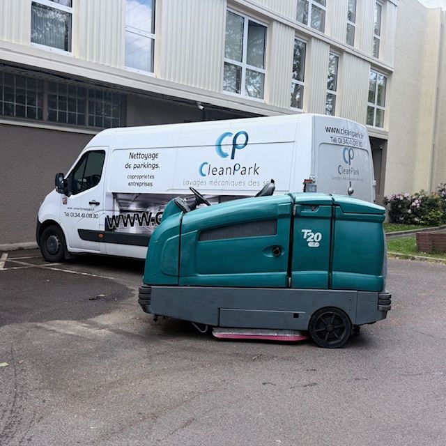 Une balayeuse de rue turquoise est garée à côté d'une camionnette blanche CleanPark devant un bâtiment.
