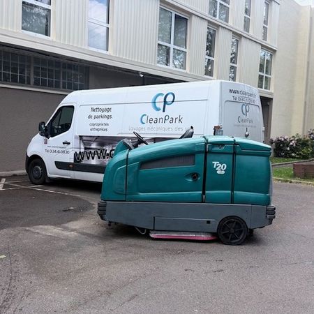 Une balayeuse de rue turquoise est garée à côté d'une camionnette blanche CleanPark devant un bâtiment.