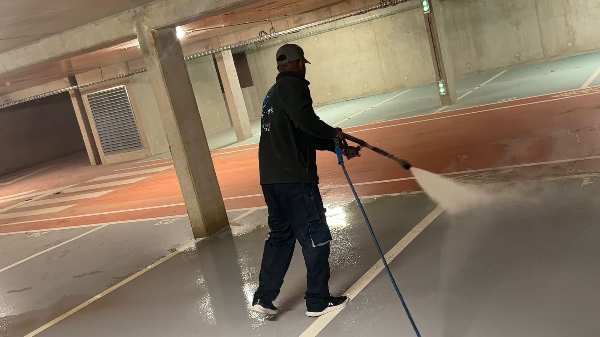 Personne vêtue de sombre, tenant une canne, dans un parking souterrain aux voies peintes.