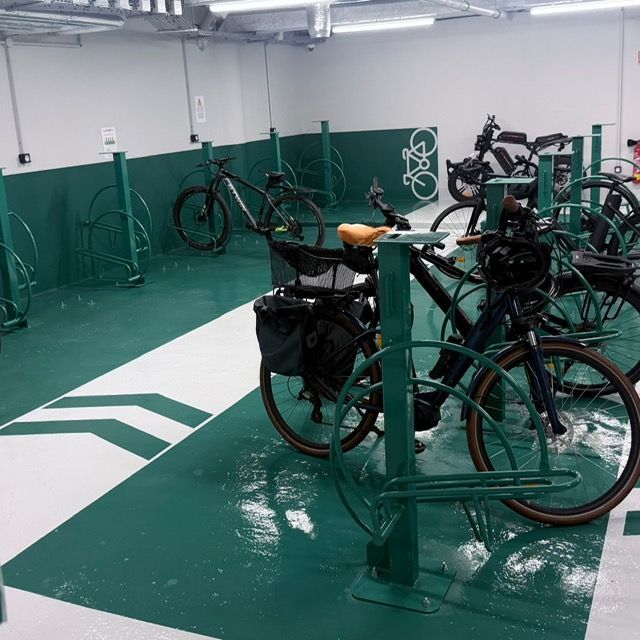 Vélos garés dans un local à vélos intérieur vert, aux murs blancs et au marquage au sol.