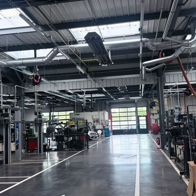 Atelier de réparation automobile vide, avec ponts élévateurs, outils et un sol en béton brillant sous des puits de lumière.