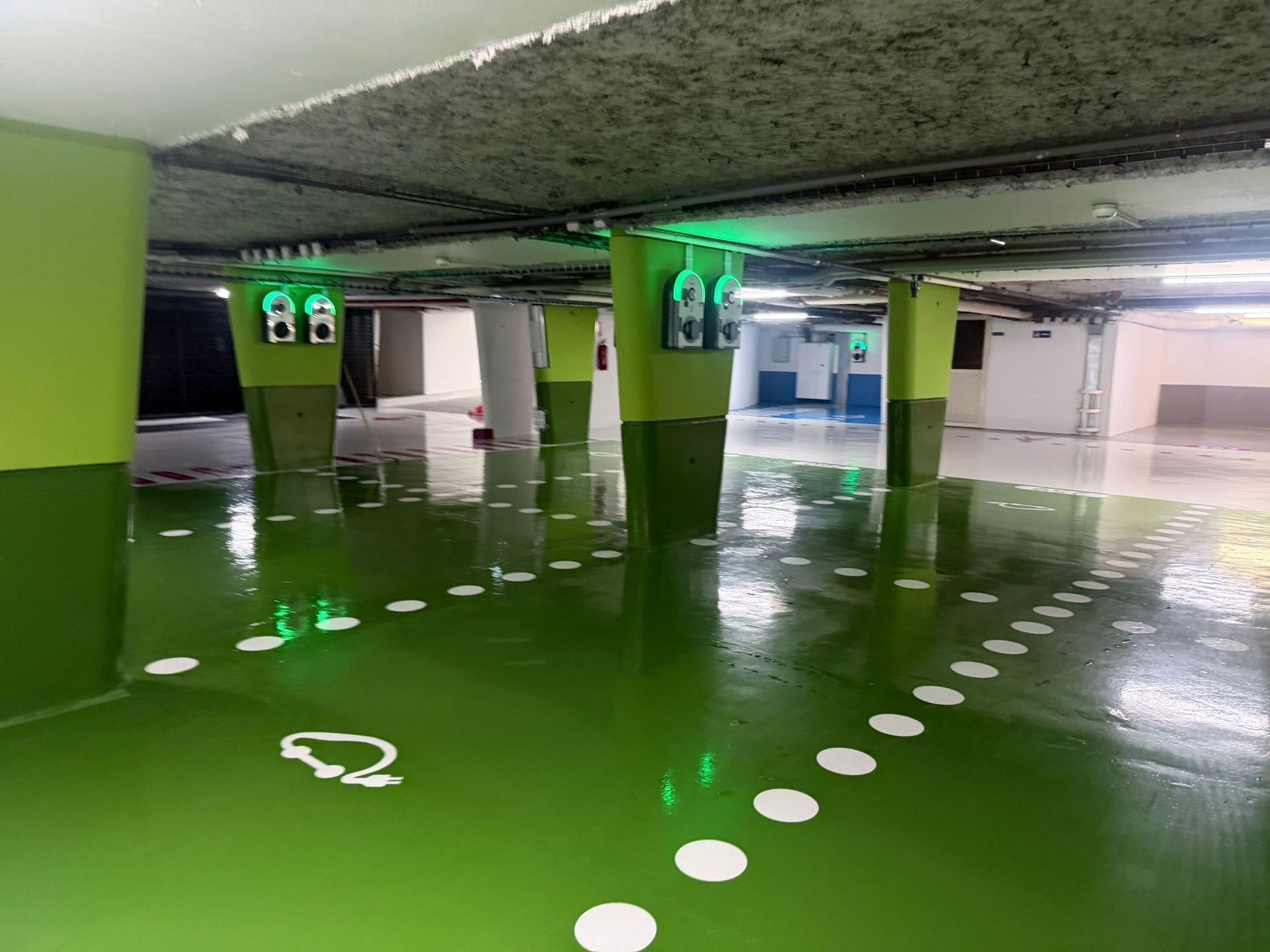 Parking intérieur vide avec sol vert brillant, marquages ​​de voies en pointillés blancs et plafond bas en béton