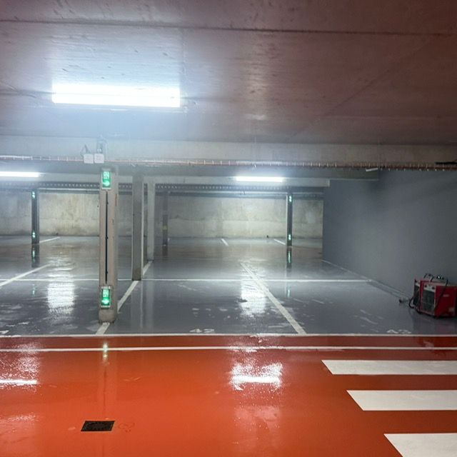 Parking souterrain vide, sol en béton mouillé, marquages ​​orange au sol et bandes blanches sous éclairage fluorescent