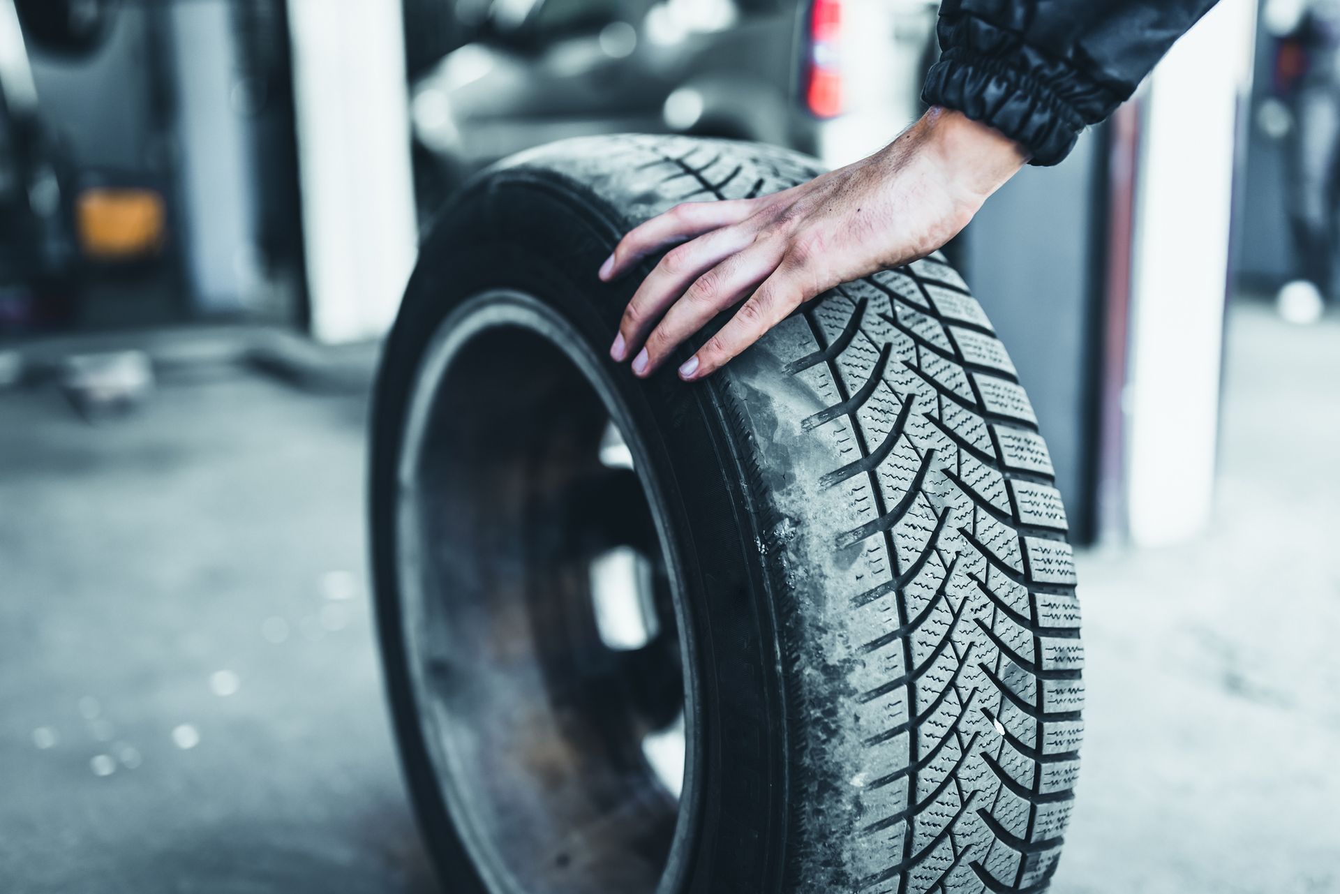 A car service worker’s hand rolls a tyre on the floor of a car shop. 