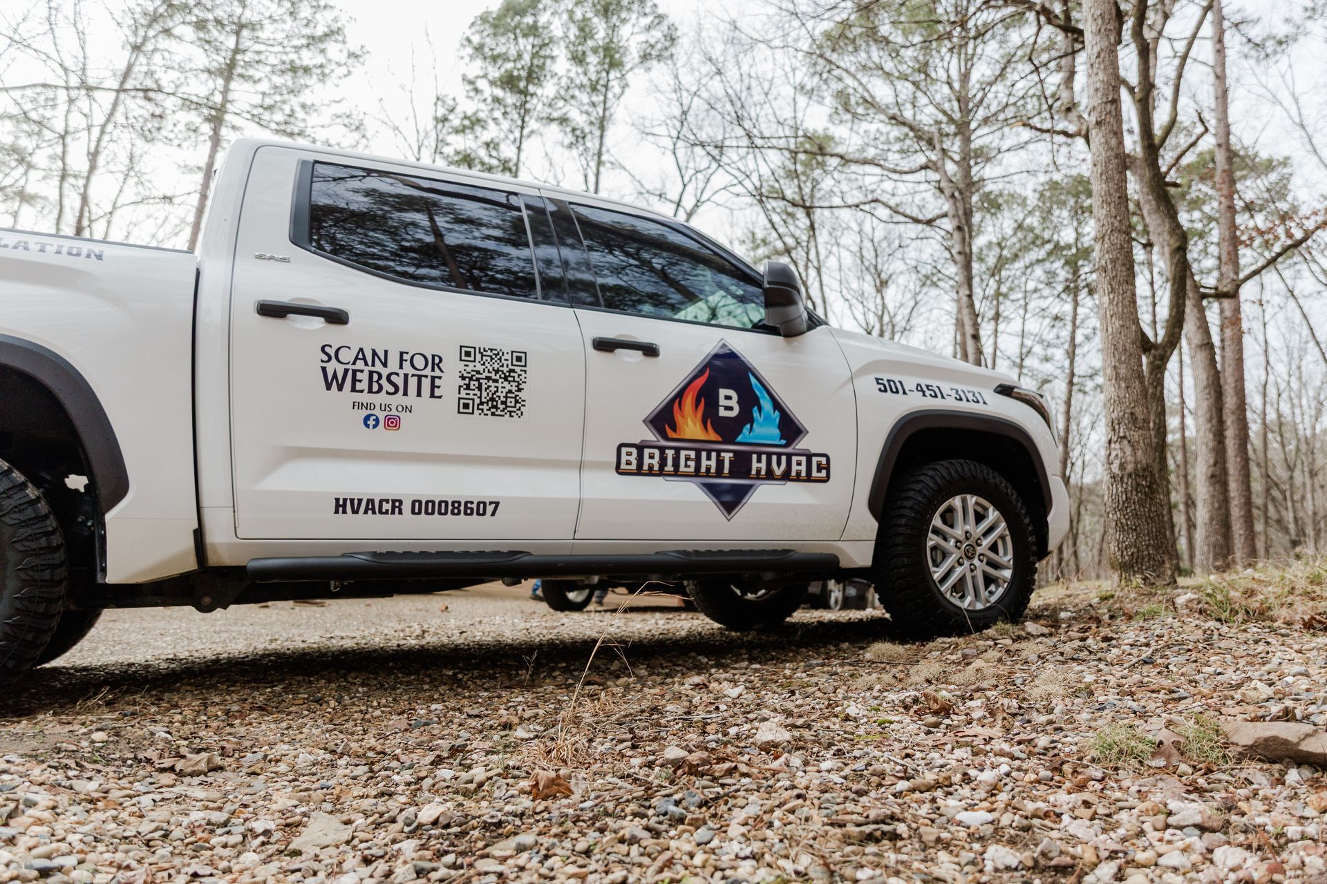 White pickup truck with company logos parked on a leaf-covered forest trail